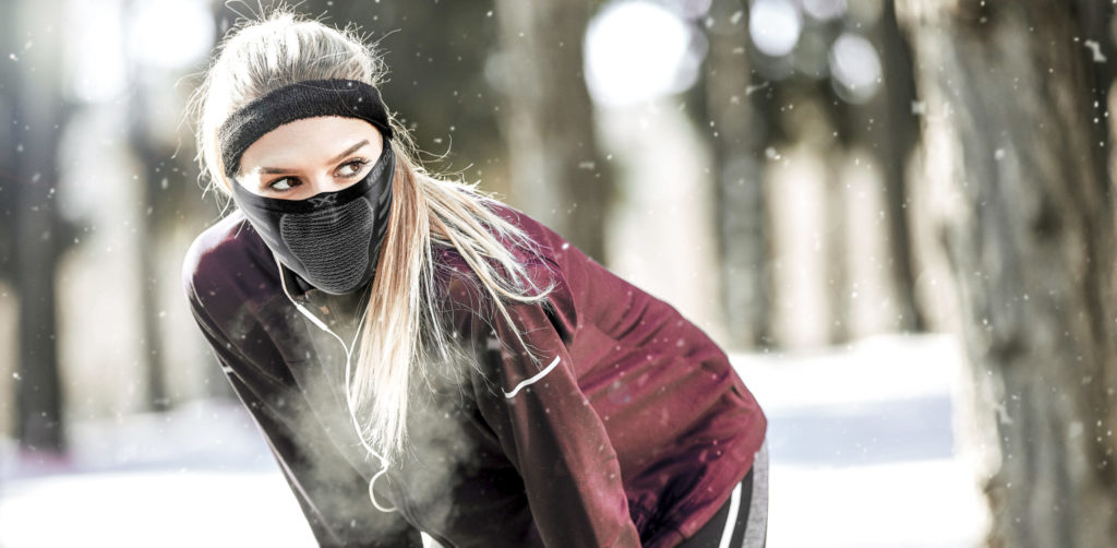 Female runner wearing NAROO sports mask X9 mask is bent over catching her breath in winter.